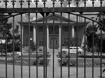 Movie still from “Harvey” (1950), directed by Henry Koster – A black - and - white photo of a house behind a fence; Extreme Wide shot, Low angle