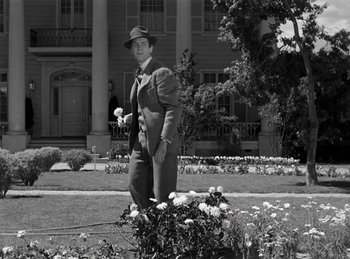 Movie still from “Harvey” (1950), directed by Henry Koster – A black and white photo of a man standing in front of a flower bed; Wide shot, Low angle