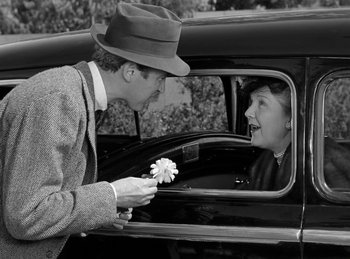 Movie still from “Harvey” (1950), directed by Henry Koster – A man giving a flower to a woman sitting in the back of a car; Medium shot, Over the shoulder angle