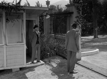 Movie still from “Harvey” (1950), directed by Henry Koster – Two men standing outside of a building in a yard; Wide shot, Low angle