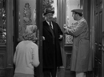 Movie still from “Harvey” (1950), directed by Henry Koster – A man in a hat and a coat is standing in front of two other men; Medium shot, Over the shoulder angle