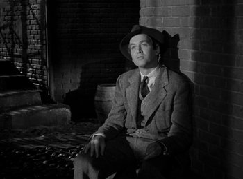 Movie still from “Harvey” (1950), directed by Henry Koster – A man in a suit and hat sitting on a brick wall; Medium shot, High angle