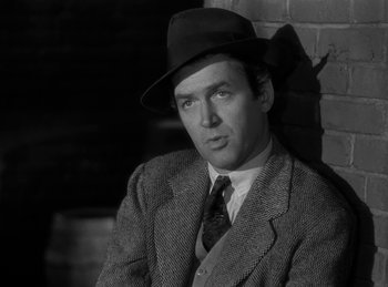 Movie still from “Harvey” (1950), directed by Henry Koster – A man wearing a suit and a hat sitting in front of a brick wall; Close Up shot, Low angle
