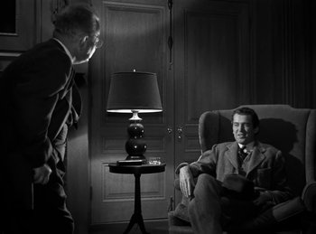 Movie still from “Harvey” (1950), directed by Henry Koster – A man in a suit and tie sitting next to a man in a chair; Medium shot, Over the shoulder angle