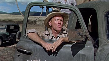 Movie still from “Hatari!” (1962), directed by Howard Hawks – A man sitting in the driver's seat of an old truck; Medium shot, Low angle