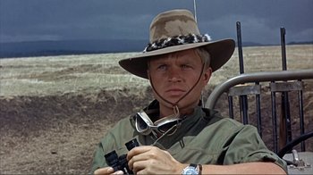 Movie still from “Hatari!” (1962), directed by Howard Hawks – A man with a hat and sunglasses holding a cell phone; Close Up shot, Low angle