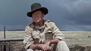 Movie still from “Hatari!” (1962), directed by Howard Hawks – An older man wearing a hat sitting in a field; Medium shot, Low angle