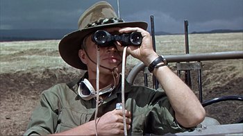 Movie still from “Hatari!” (1962), directed by Howard Hawks – A man in a hat looking through a pair of binoculars; Medium shot, Low angle