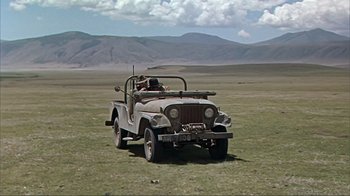 Movie still from “Hatari!” (1962), directed by Howard Hawks – An old jeep is parked in the middle of a field; Extreme Wide shot, High angle