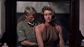 Movie still from “Hatari!” (1962), directed by Howard Hawks – A man and a woman are standing next to each other in front of a microphone; Medium shot, Over the shoulder angle