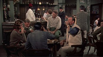 Movie still from “Hatari!” (1962), directed by Howard Hawks – A group of men sitting at a table in a room; Wide shot, High angle