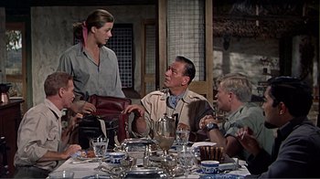 Movie still from “Hatari!” (1962), directed by Howard Hawks – A group of people sitting around a table with plates; Medium shot, Over the shoulder angle