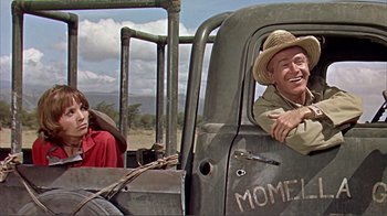 Movie still from “Hatari!” (1962), directed by Howard Hawks – An older man and woman in the back of an old truck; Medium shot, Over the shoulder angle