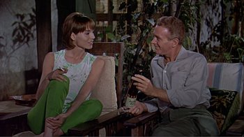 Movie still from “Hatari!” (1962), directed by Howard Hawks – A man and a woman sitting on a chair holding wine bottles; Medium shot, High angle
