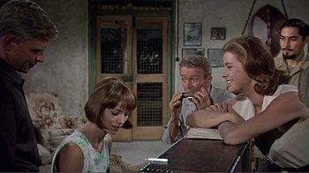 Movie still from “Hatari!” (1962), directed by Howard Hawks – A group of people sitting around a table; Medium shot, Over the shoulder angle