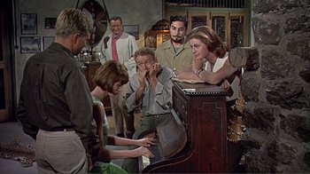 Movie still from “Hatari!” (1962), directed by Howard Hawks – A group of people standing around a piano; Medium shot, High angle