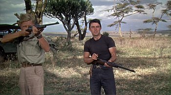 Movie still from “Hatari!” (1962), directed by Howard Hawks – A man holding a rifle while standing next to another man holding a rifle; Medium shot, Low angle