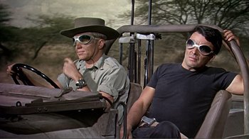 Movie still from “Hatari!” (1962), directed by Howard Hawks – Two men sitting in the back of a vehicle; Medium shot, Low angle