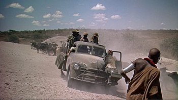 Movie still from “Hatari!” (1962), directed by Howard Hawks – A group of men riding in a truck down a dirt road; Wide shot, Low angle