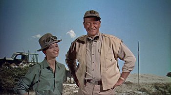 Movie still from “Hatari!” (1962), directed by Howard Hawks – A man standing next to a woman wearing a hat; Medium shot, Low angle