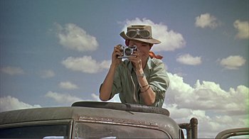 Movie still from “Hatari!” (1962), directed by Howard Hawks – A woman taking a picture with a camera on top of a car; Medium shot, Low angle