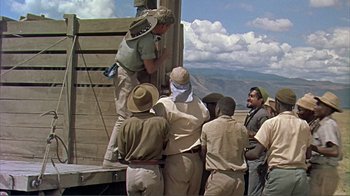Movie still from “Hatari!” (1962), directed by Howard Hawks – A group of men standing next to each other on a platform; Wide shot, Over the shoulder angle