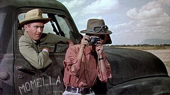 Movie still from “Hatari!” (1962), directed by Howard Hawks – A man taking a picture with a camera in front of an old truck; Medium shot, Low angle