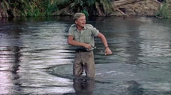 Movie still from “Hatari!” (1962), directed by Howard Hawks – A man standing in the water holding a fishing rod; Medium shot, Low angle