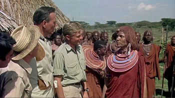 Movie still from “Hatari!” (1962), directed by Howard Hawks – A group of people standing around each other in front of a crowd; Medium shot, Over the shoulder angle