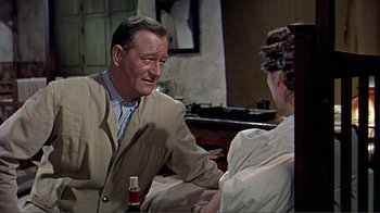 Movie still from “Hatari!” (1962), directed by Howard Hawks – An older man sitting at a table talking to a young woman; Medium shot, Over the shoulder angle