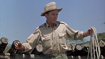 Movie still from “Hatari!” (1962), directed by Howard Hawks – A man wearing a hat standing in front of logs; Medium shot, Low angle