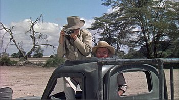 Movie still from “Hatari!” (1962), directed by Howard Hawks – A man taking a picture of another man sitting in the back of a truck; Medium shot, Over the shoulder angle