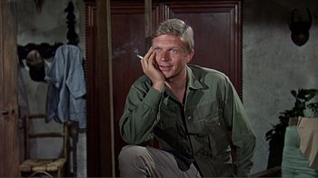 Movie still from “Hatari!” (1962), directed by Howard Hawks – A man sitting in front of a wall smoking a cigarette; Close Up shot, High angle