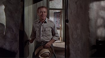 Movie still from “Hatari!” (1962), directed by Howard Hawks – A man standing in front of a door wearing a hat; Medium shot, Over the shoulder angle