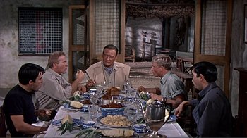 Movie still from “Hatari!” (1962), directed by Howard Hawks – A group of men sitting around a table eating food; Wide shot, Over the shoulder angle