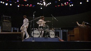Movie still from “Head” (1968), directed by Bob Rafelson – A couple of people that are playing drums on a stage; Wide shot, Low angle