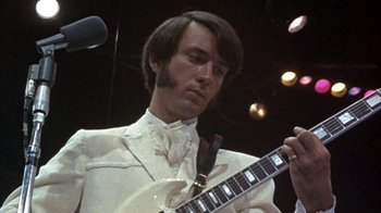 Movie still from “Head” (1968), directed by Bob Rafelson – A man in a white suit holding a white guitar; Close Up shot, Low angle