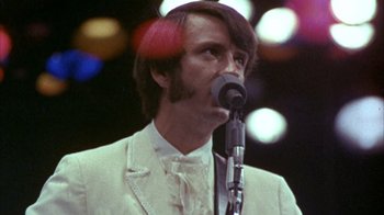 Movie still from “Head” (1968), directed by Bob Rafelson – A man in a white suit is speaking into a microphone; Close Up shot, Low angle