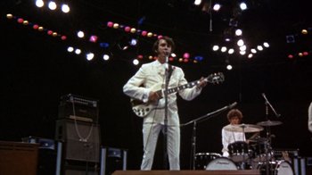 Movie still from “Head” (1968), directed by Bob Rafelson – A man in a white suit is playing a guitar; Wide shot, Low angle