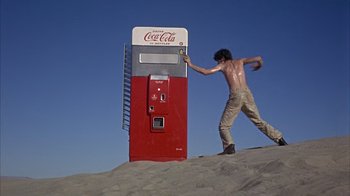 Movie still from “Head” (1968), directed by Bob Rafelson – A man is standing next to an old coke machine; Wide shot, Low angle