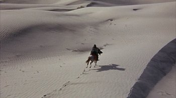 Movie still from “Head” (1968), directed by Bob Rafelson – A man riding a horse through the sand dunes; Extreme Wide shot, High angle