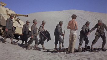 Movie still from “Head” (1968), directed by Bob Rafelson – A group of men standing on top of a sandy hill; Wide shot, Low angle