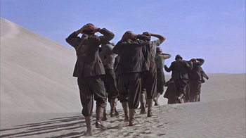 Movie still from “Head” (1968), directed by Bob Rafelson – A group of men walking across a sandy beach; Wide shot, Low angle