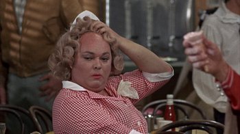 Movie still from “Head” (1968), directed by Bob Rafelson – An older woman with blonde curly hair is holding her head; Close Up shot, Over the shoulder angle