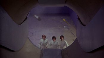 Movie still from “Head” (1968), directed by Bob Rafelson – Three young people standing in a room with a purple background; Wide shot, Overhead angle
