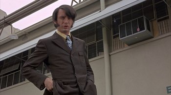 Movie still from “Head” (1968), directed by Bob Rafelson – A man wearing a suit and tie standing outside; Medium shot, Low angle
