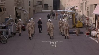 Movie still from “Head” (1968), directed by Bob Rafelson – A group of men in uniform are standing in the middle of the street; Wide shot, High angle