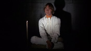 Movie still from “Head” (1968), directed by Bob Rafelson – A man sitting in the middle of a room with a lit candle; Medium shot, Low angle