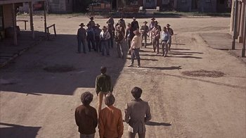 Movie still from “Head” (1968), directed by Bob Rafelson – A group of people standing in the middle of a dirt field; Wide shot, High angle