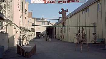 Movie still from “Head” (1968), directed by Bob Rafelson – A man standing on top of a pole in the middle of a street; Wide shot, Low angle